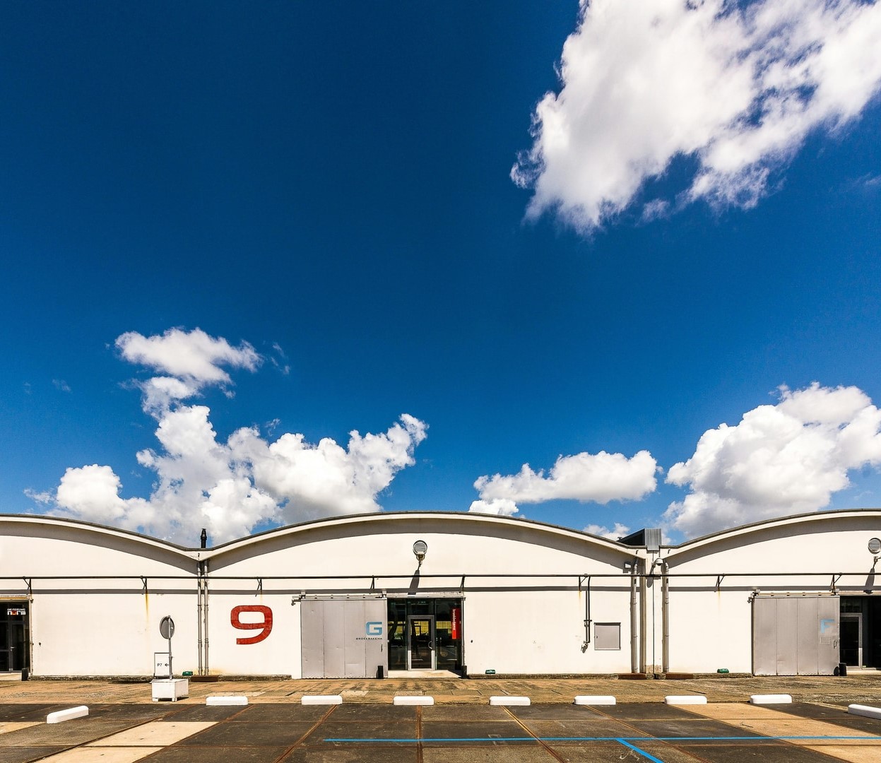 3 large warehouses with large concrete areas in front of their open door entrances, and bright blue sky.