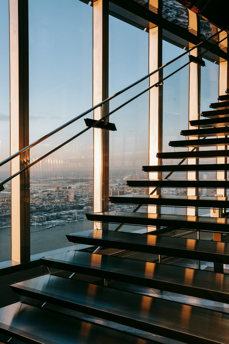 Modern staircase in an office with floor to ceiling glass windows and the City of London skyline.